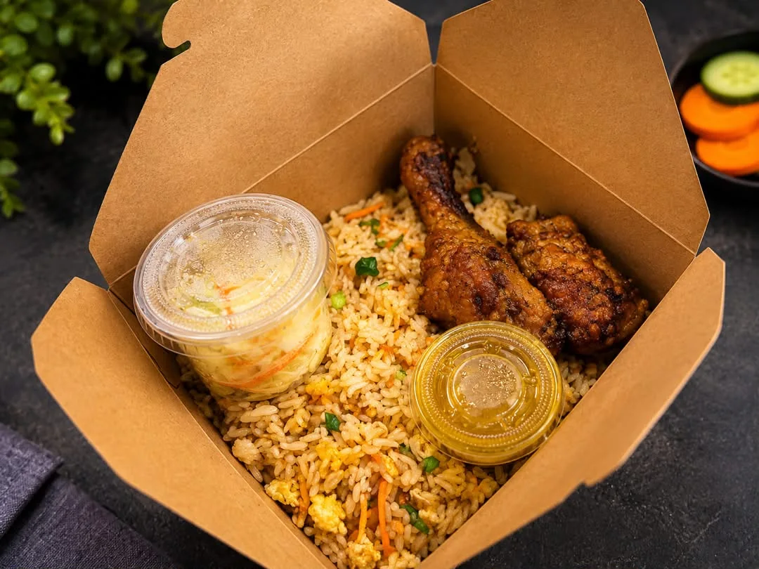 Takeaway box packed with fried rice, two pieces of chicken, coleslaw and sauce cups